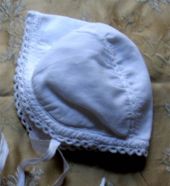 Pair of white cotton newborn baby bonnets.